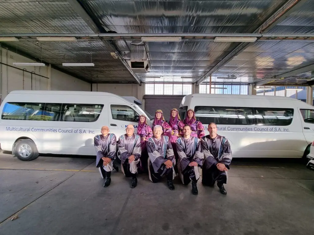 group of people in Lebanese cultural dress, in front of 2 MCCSA mini bus / vans