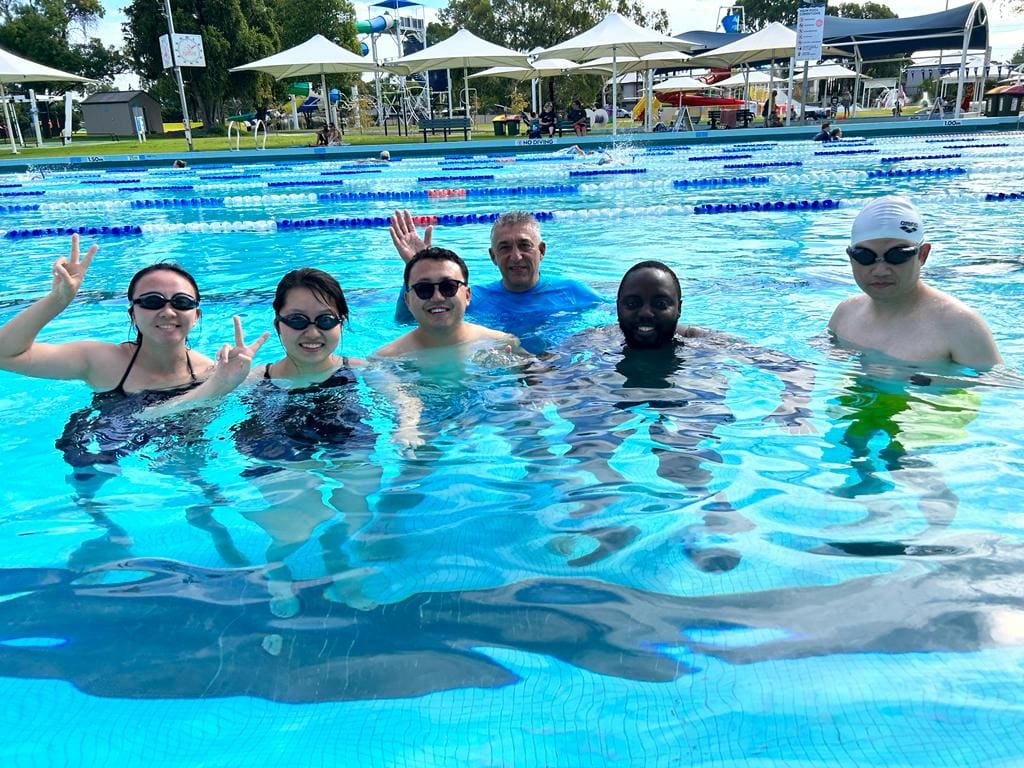 6 people in a swimming pool, smiling at the camera 